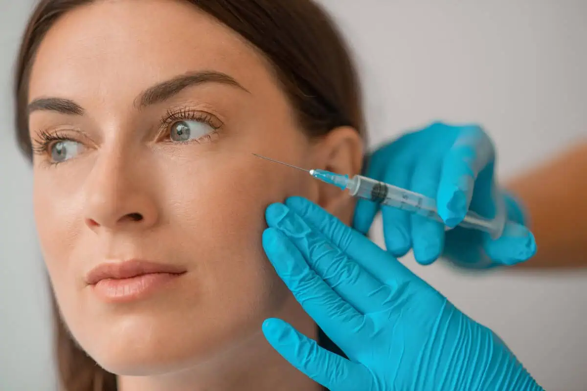 Woman receiving wrinkle relaxer injection near eye by a gloved professional at a medical aesthetic clinic in Laguna Hills, CA.